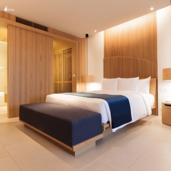 A minimalist bedroom with natural wood accents, a white bed adorned with a navy throw, and a cushioned bench at the foot of the bed.