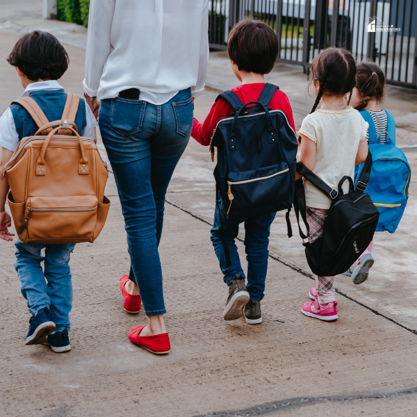 A group of young children with backpacks walking alongside an adult, symbolizing family outings and shared adventures.