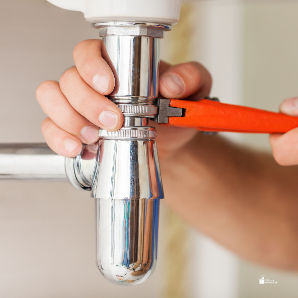 Hands using a wrench to tighten a pipe connection under a sink, showcasing simple plumbing tips for reducing water bills and repair costs.