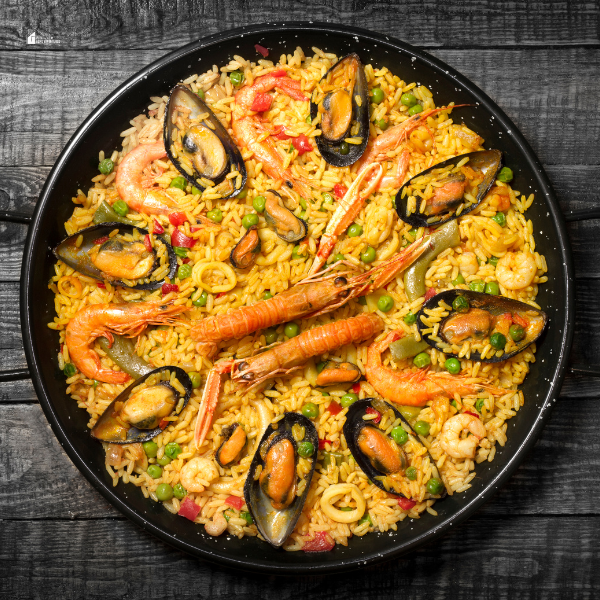 Overhead view of a large skillet filled with colorful Spanish paella, topped with shrimp, mussels, peas, and saffron rice.