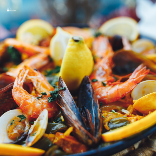 Close-up of a seafood paella dish with shrimp, mussels, clams, and lemon wedges arranged on a plate.