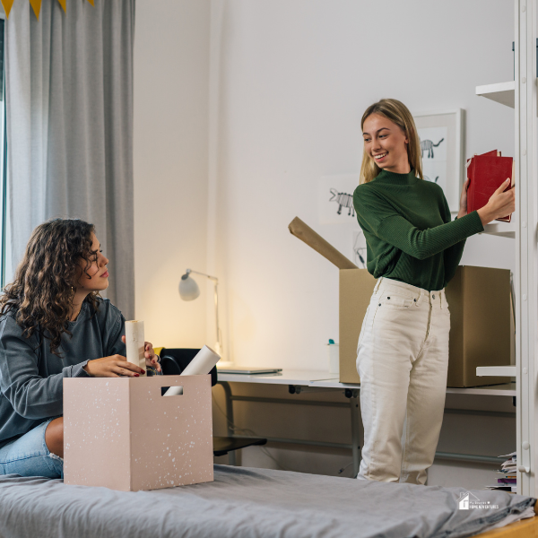 Two women organizing belongings in a shared room, depicting the process of settling in with new roommates.