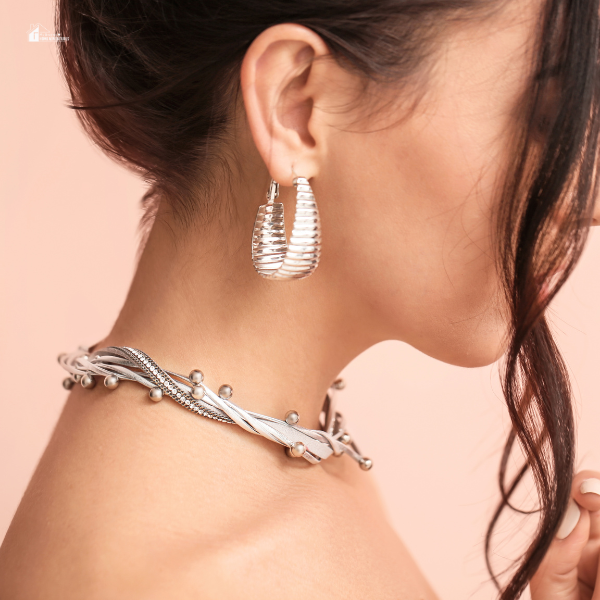 A side profile of a woman wearing a silver statement necklace and textured earrings, showcasing elegant luxury jewelry trends for 2024.