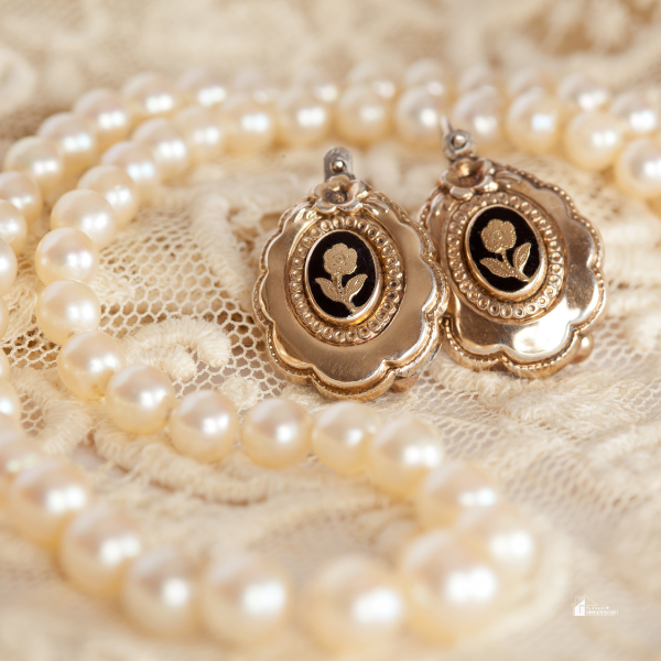 A pair of vintage gold floral earrings placed on delicate lace alongside a classic pearl necklace, highlighting timeless luxury jewelry trends for 2024.