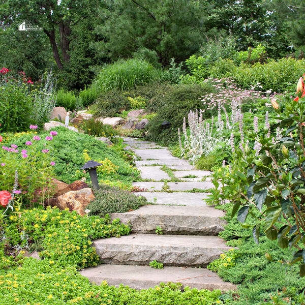 A stone pathway winding through a garden filled with greenery and colorful flowers, illustrating the use of functional landscaping to design an easy-to-manage outdoor space.