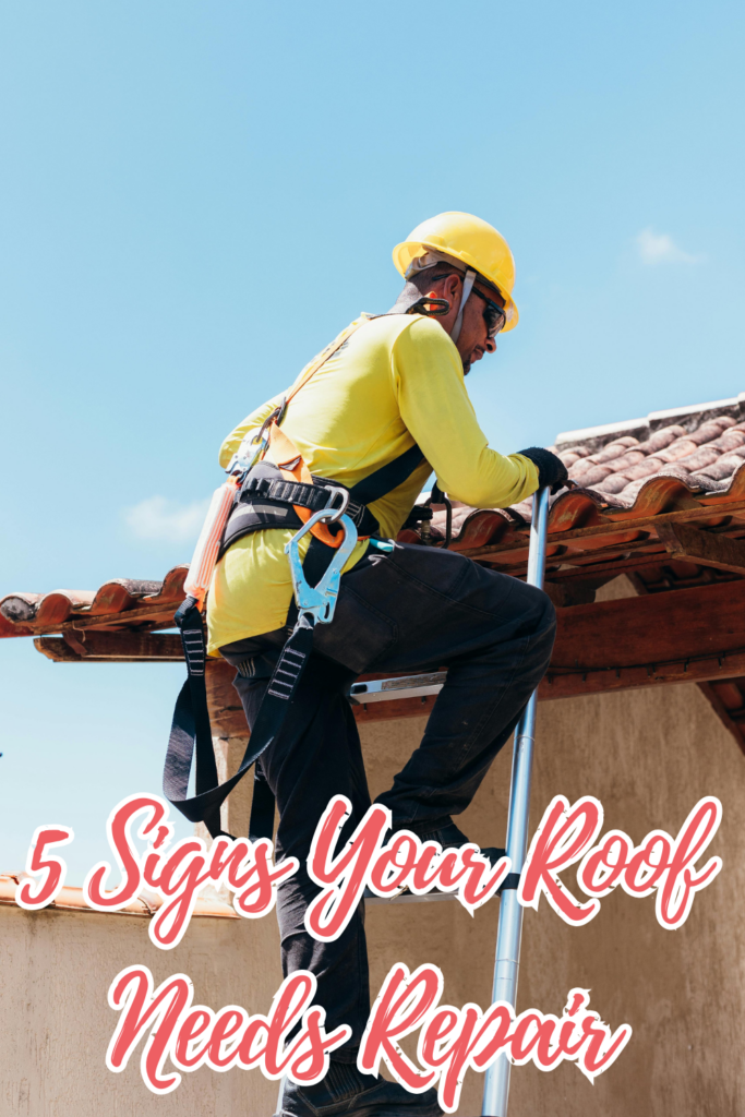 A construction worker wearing a yellow hard hat and safety harness climbs a ladder to inspect a roof under a clear blue sky.