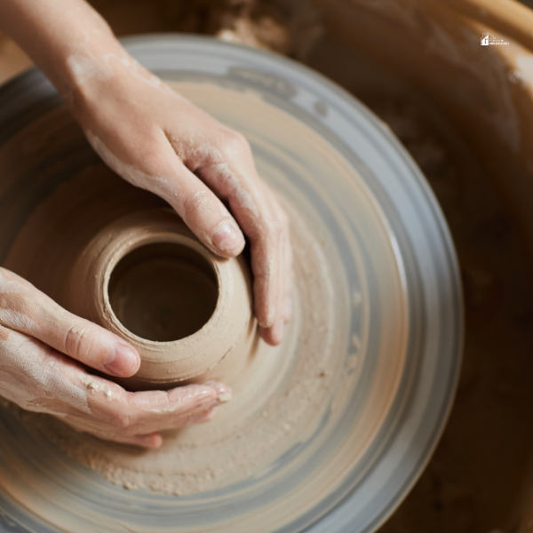 Hands shaping a clay pot on a spinning pottery wheel in a workshop.