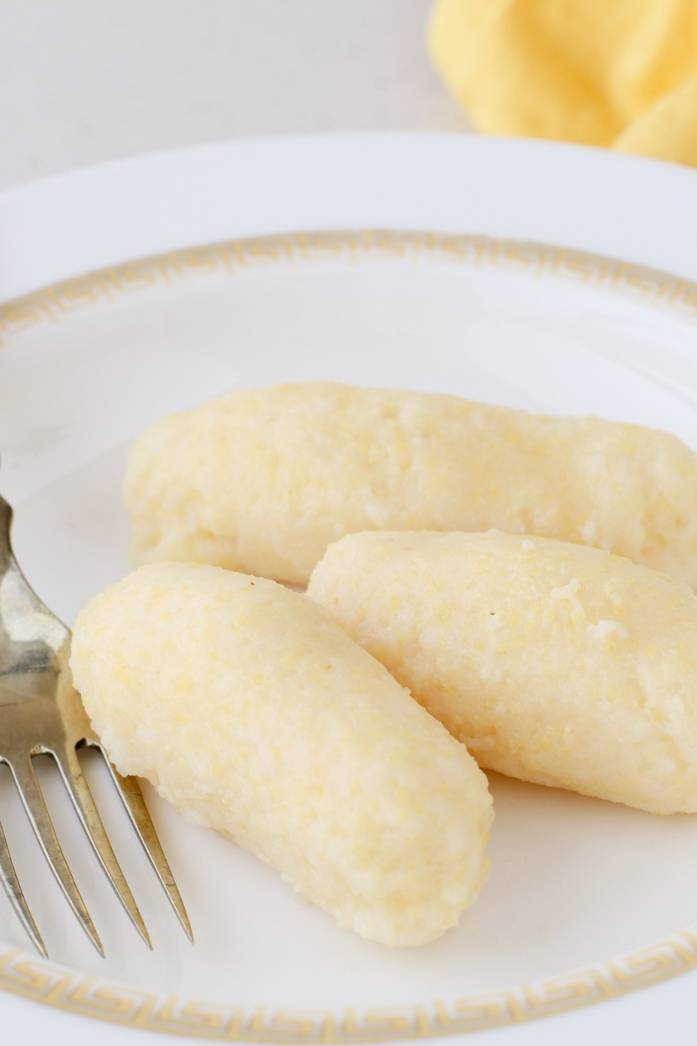 A close-up of freshly made Puerto Rican guanimes, traditional cornmeal dumplings, served on a decorative white plate with a fork, showcasing their soft texture and authentic homemade appearance.