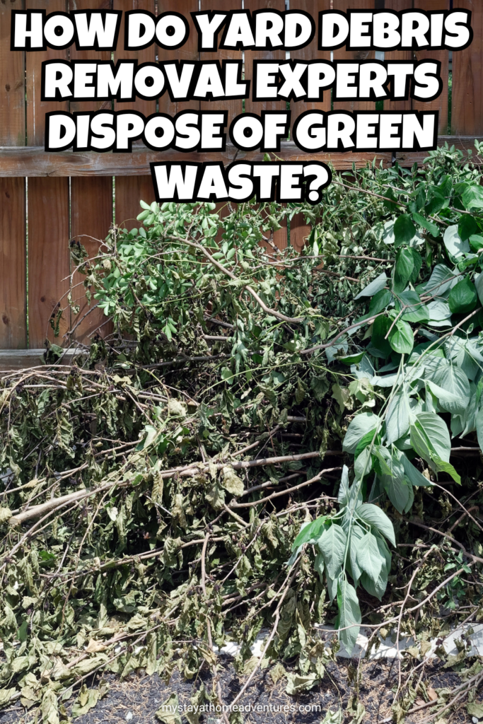 A large pile of freshly cut green branches and leaves stacked against a wooden fence, awaiting removal or disposal.