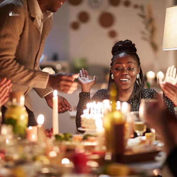 A joyful woman sitting at a beautifully decorated table, surrounded by friends as she prepares to blow out candles on her birthday cake.