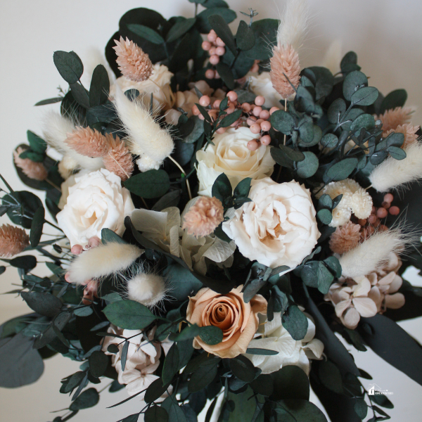 A detailed bouquet featuring white and peach roses, eucalyptus leaves, and dried floral elements, arranged in a soft, rustic style.