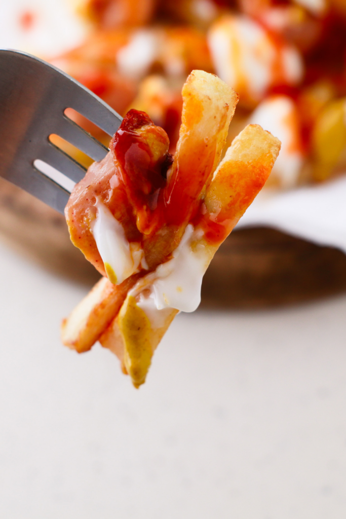 A close-up of a fork holding crispy fries and hot dog slices drizzled with ketchup, mayonnaise, and mustard, showcasing the vibrant flavors of a classic Salchipapas recipe.