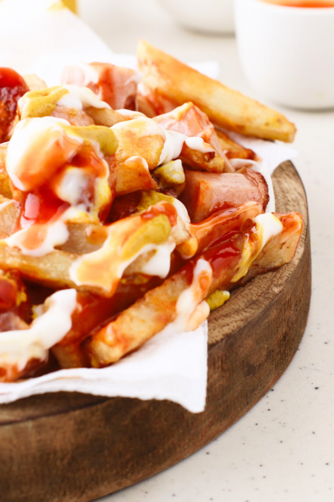 A wooden plate filled with Salchipapas, featuring golden fries, hot dog slices, and a mix of vibrant toppings like ketchup, mayonnaise, and mustard, highlighting a classic Peruvian street food.