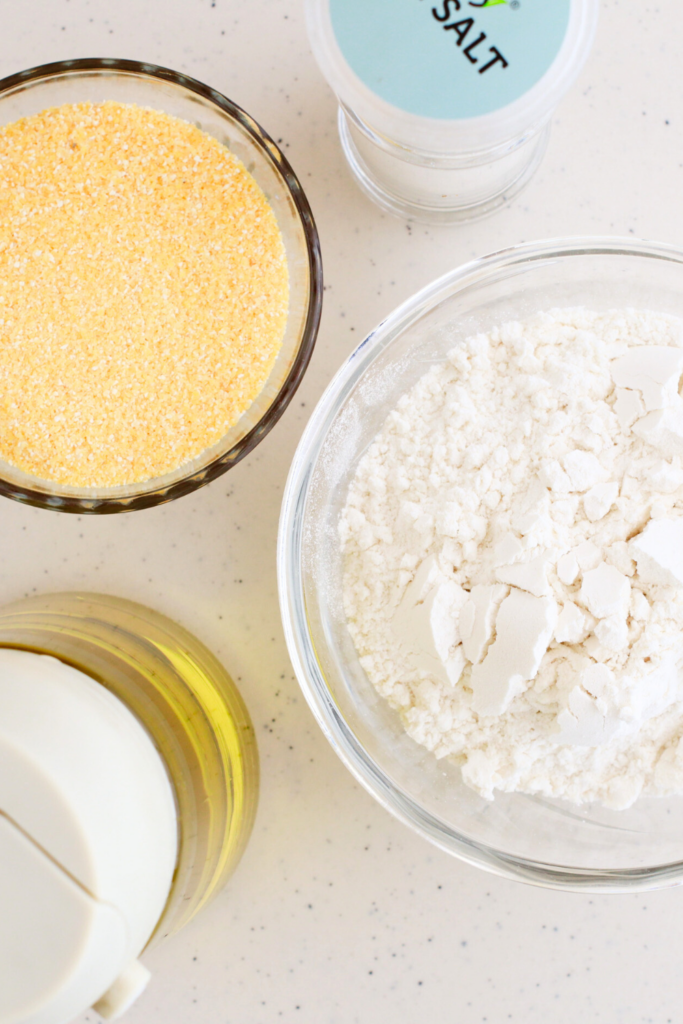 A top-down view of key ingredients for making Puerto Rican guanimes, including cornmeal, all-purpose flour, olive oil, and salt—simple pantry staples used to create this traditional Puerto Rican side dish.