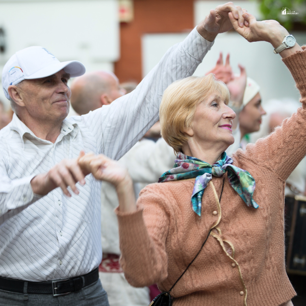 A smiling elderly couple dancing outdoors, enjoying an active and joyful moment.