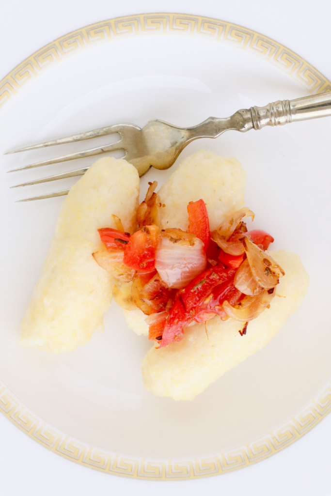 A plated serving of Puerto Rican guanimes topped with sautéed onions, tomatoes, and peppers, highlighting the traditional cornmeal dumplings' soft texture and their perfect pairing with savory toppings.