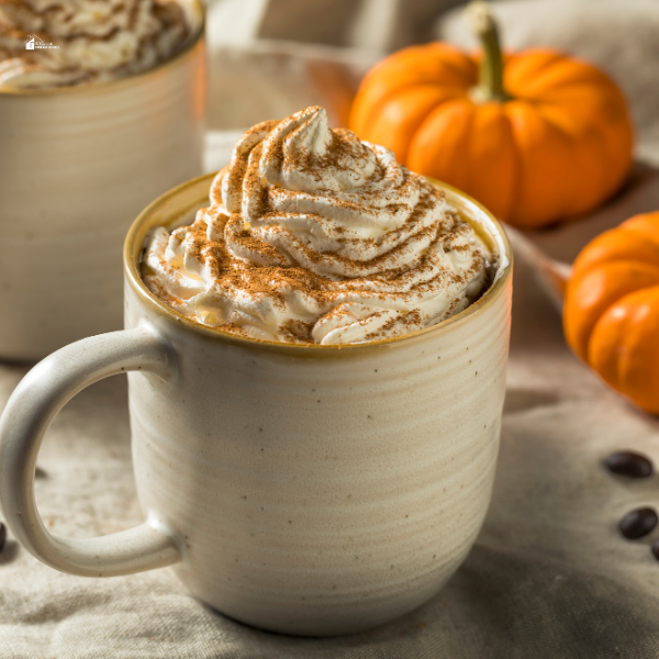 A warm mug of pumpkin spice latte topped with whipped cream and cinnamon, surrounded by small pumpkins on a cozy autumn table setting.