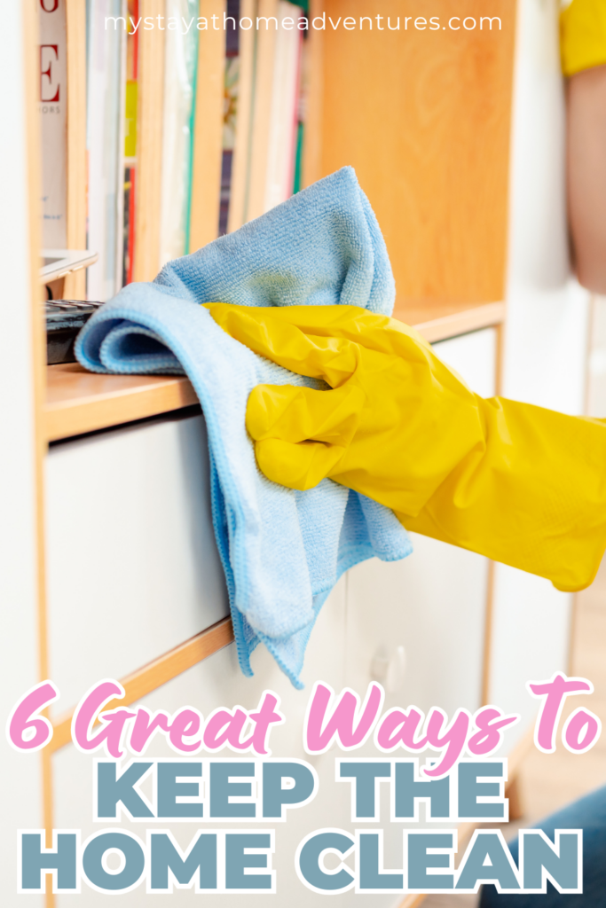 A person wearing yellow gloves uses a blue cloth to clean a bookshelf in a tidy home environment.