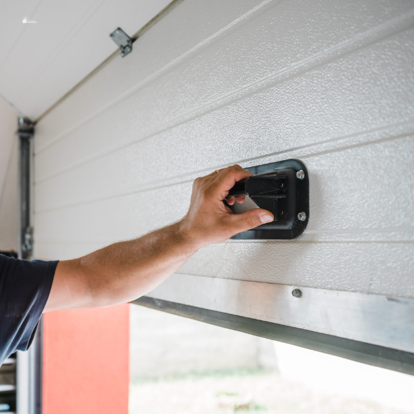 A close-up of a person's hand gripping the handle of a white garage door as they manually open or close it.