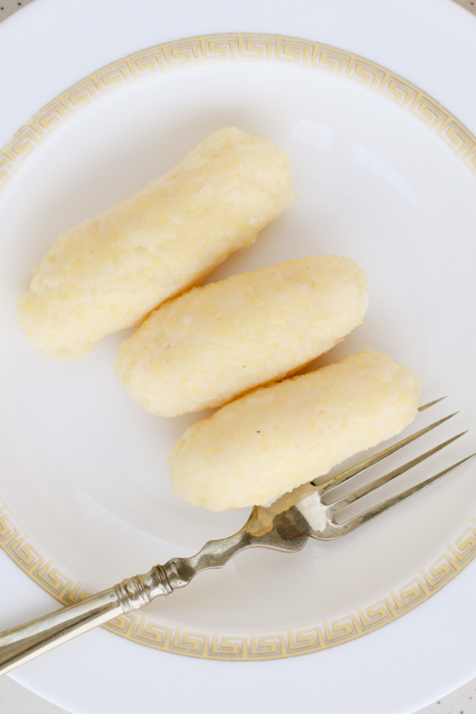 A close-up of three Puerto Rican guanimes, traditional cornmeal dumplings, served on a white plate with a decorative gold rim, showcasing their smooth, firm texture—perfect for pairing with stews and classic Puerto Rican side dishes.