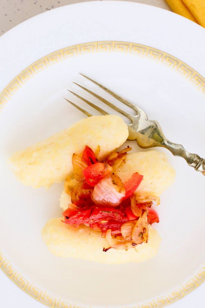 A close-up of Puerto Rican guanimes served with sautéed onions, tomatoes, and peppers on a decorative white plate, highlighting the traditional cornmeal dumplings' soft texture and rich flavors.