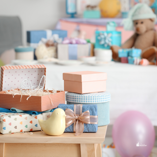 A collection of pastel-colored gift boxes, a small ceramic bird, and baby-themed decorations arranged on a table at a baby shower.