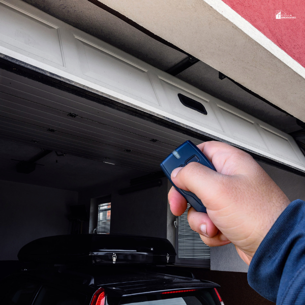 A person holding a remote control to open a white garage door with a car parked inside, illustrating modern garage door operation.