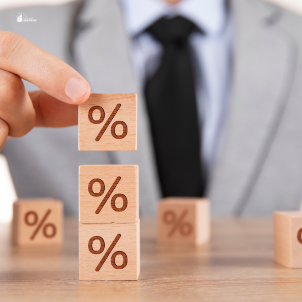 A businessperson in a suit stacks wooden blocks with percentage symbols, illustrating the concept of increasing interest rates or financial growth.