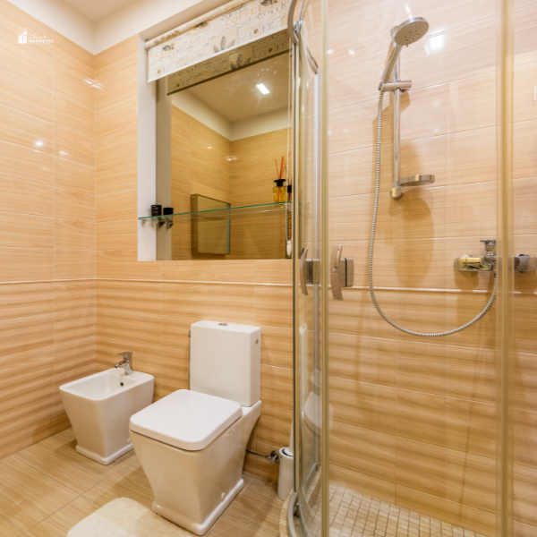 A modern small bathroom featuring beige tiled walls, a glass-enclosed shower, a white toilet, and a bidet, designed with a minimalist aesthetic.