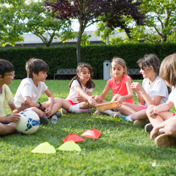 A group of kids sitting in a circle on the grass, playing games and engaging in outdoor activities on a sunny day.