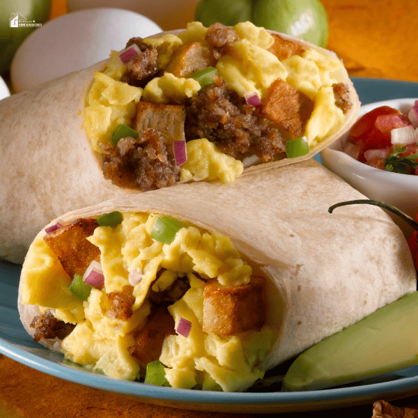 A breakfast burrito cut in half, filled with scrambled eggs, sausage, potatoes, and vegetables, with a side of salsa and avocado.