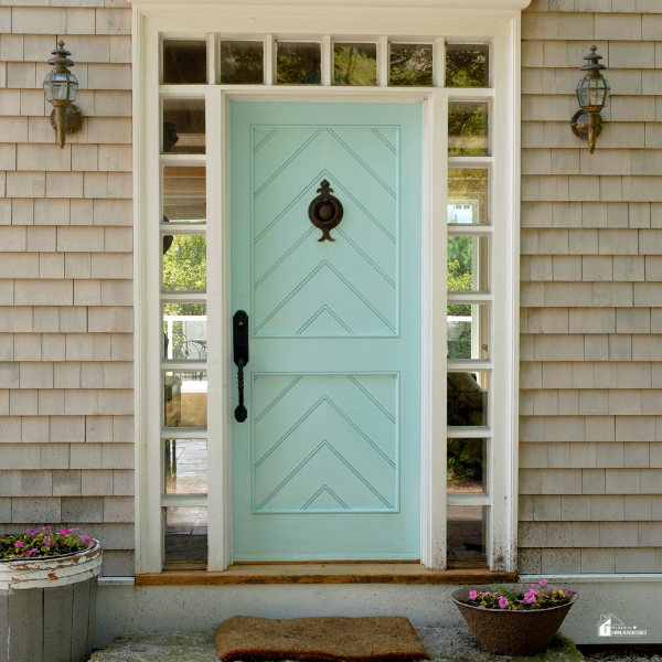 A charming light blue front door with decorative glass panels, flanked by wall-mounted lanterns and potted flowers, adding a fresh and welcoming touch to the home's entryway.