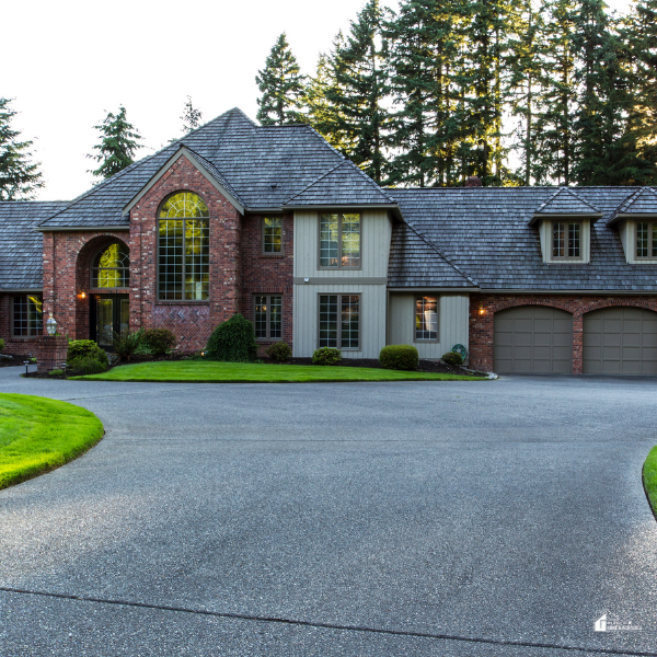 A grand brick and siding home with a well-manicured lawn, large arched windows, and an expansive driveway, highlighting elegant curb appeal and thoughtful exterior design.