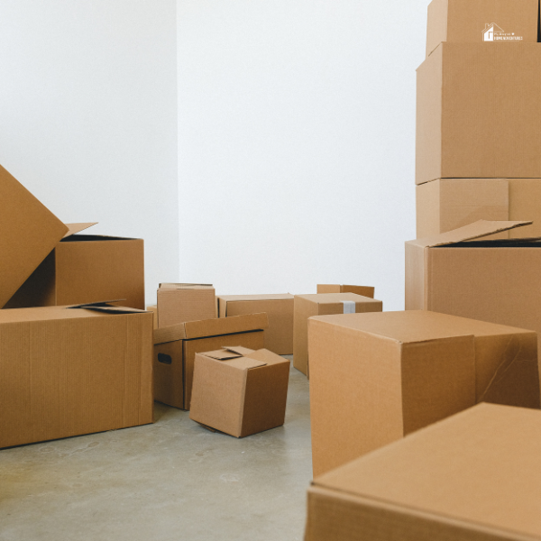 A man and woman carrying large moving boxes outside of a house, preparing for a move.