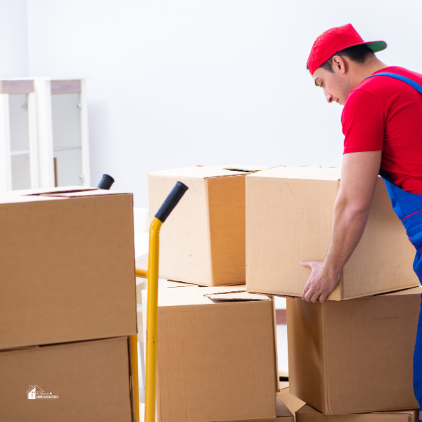 A room filled with various sizes of stacked and scattered cardboard moving boxes against a plain white wall.