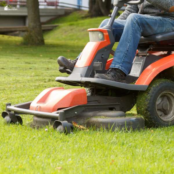 A person operates a riding lawn tractor while mowing grass.