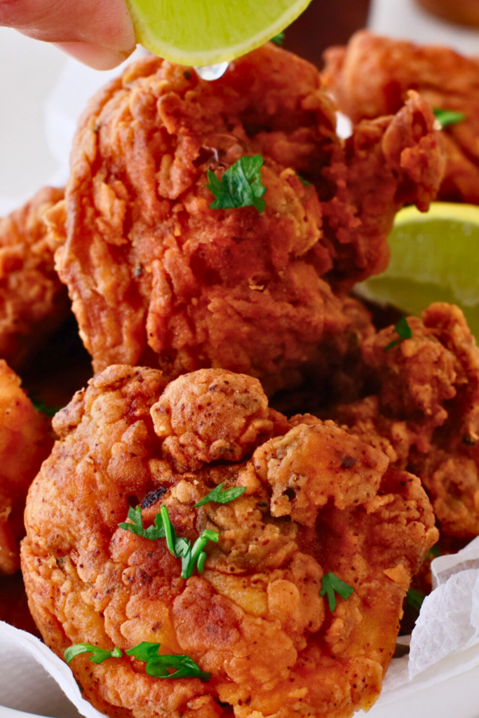 A close-up of crispy, golden-brown chicharrones de pollo, Puerto Rican fried chicken bites, garnished with fresh herbs and served with lime wedges.