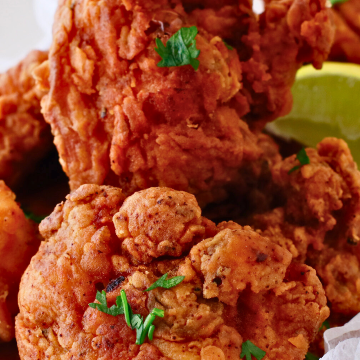 A close-up of crispy, golden-brown chicharrones de pollo, Puerto Rican fried chicken bites, garnished with fresh herbs and served with lime wedges.