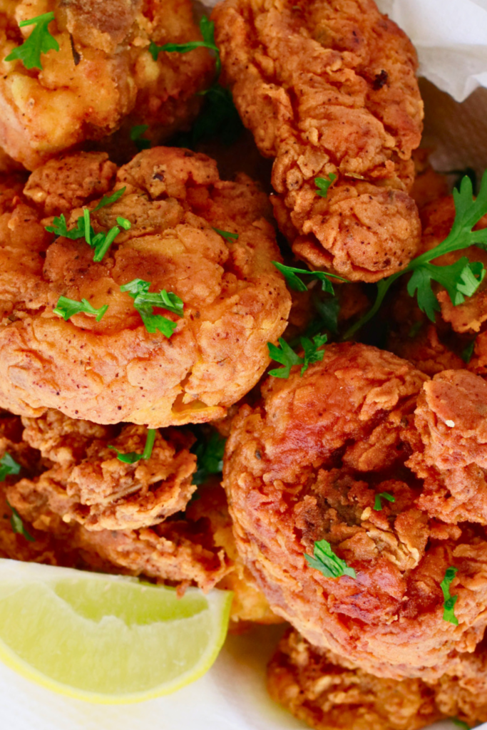 A close-up of crispy chicharrones de pollo, Puerto Rican fried chicken bites, garnished with fresh herbs and served with lime wedges for extra flavor.