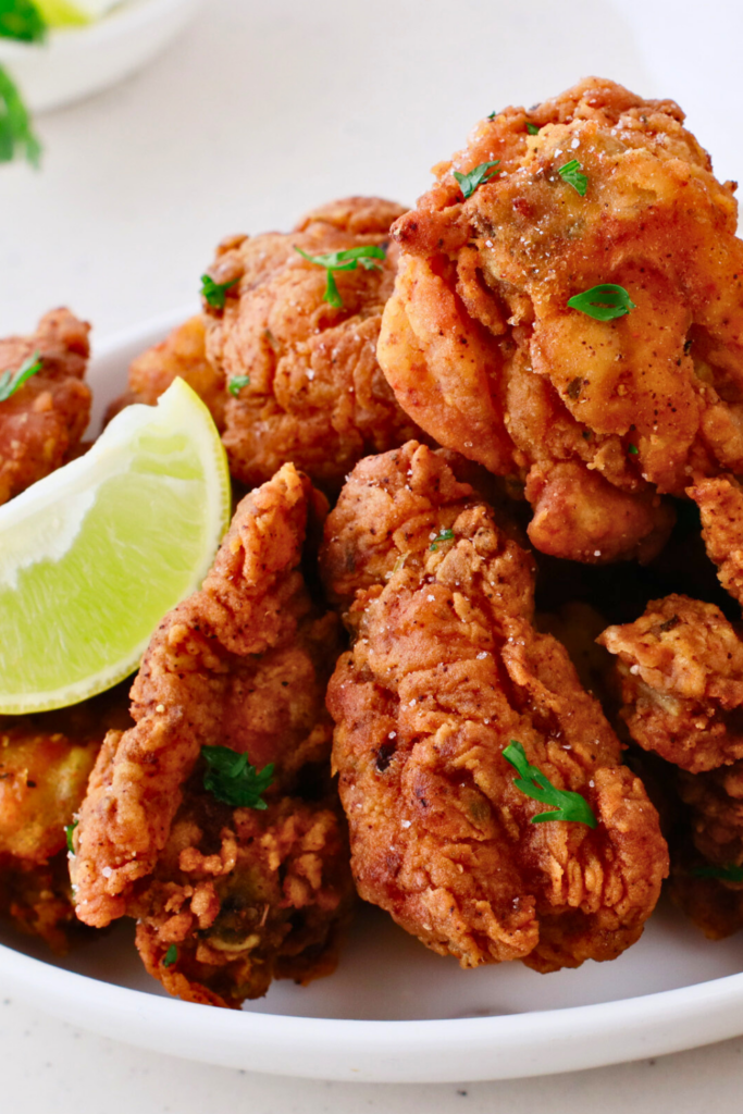 A plate of crispy chicharrones de pollo, golden-brown Puerto Rican fried chicken bites, garnished with fresh herbs and served with lime wedges.